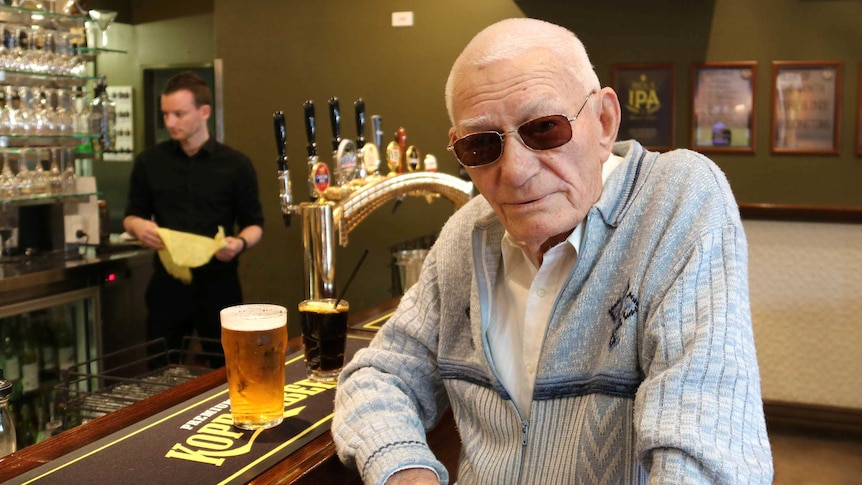 British immigrant Ernie Edwards sits at the bar with glasses on and enjoys a beer.