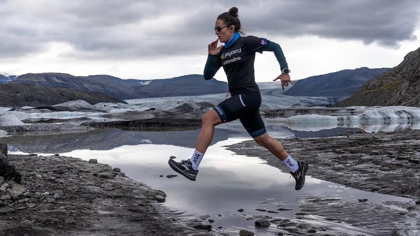 A athlete jumps over a stream of water during an ultramarathon.