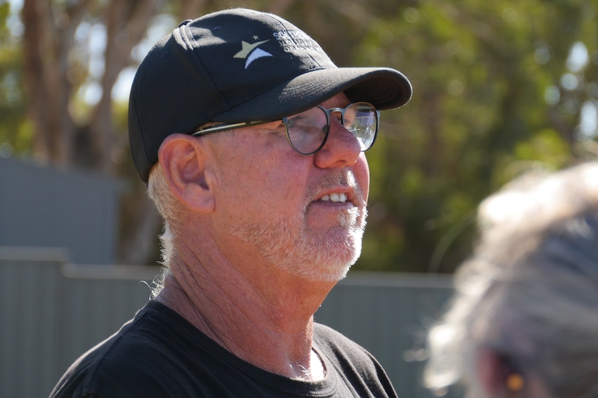 A bespectacled man in a dark cap squints in the sun.