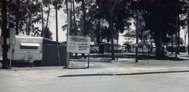 Uma imagem em preto e branco de um parque de caravanas repleto de árvores altas.