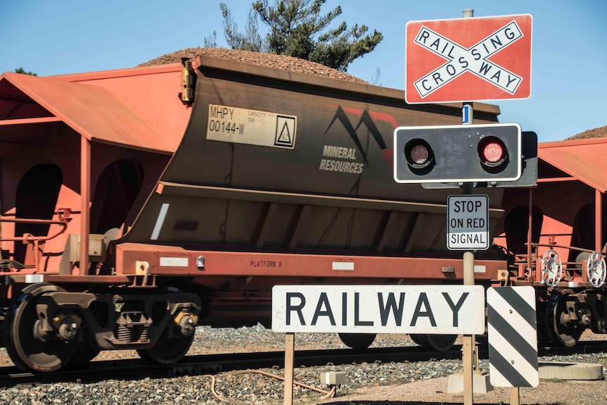 A train loaded with iron ore passes a railway crossing.  