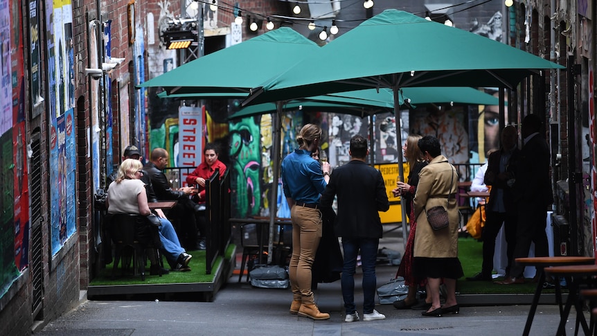 A group of people in a Melbourne laneway holding drinks and sitting down.