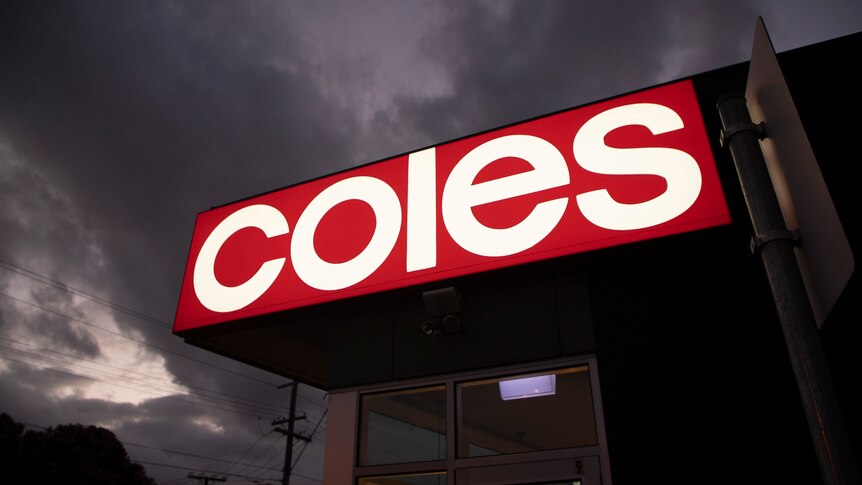 A bright red and white Coles sign at a supermarket at night.