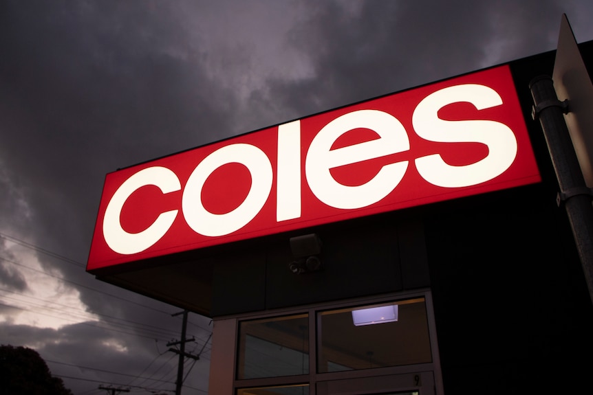 A bright red and white Coles sign at a supermarket at night.