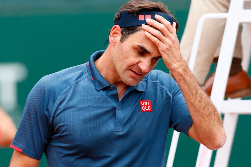 Roger Federer looks down, his hand taking off his bandana.