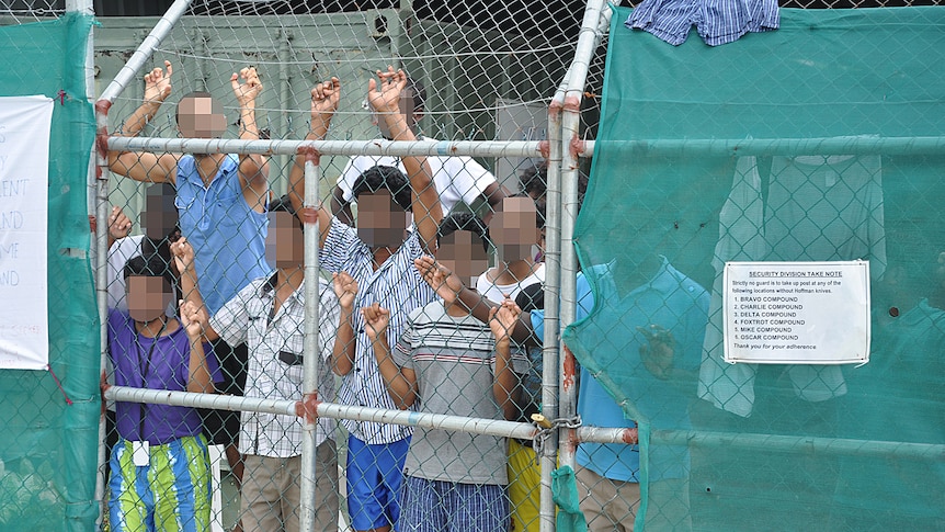 Asylum seekers stare at media from behind a fence