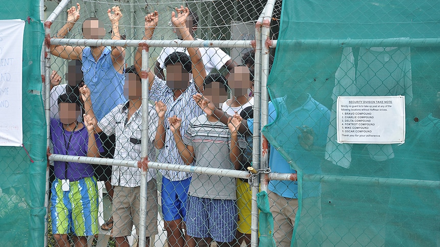 Asylum seekers stare at media from behind a fence at the Manus Island detention centre, Papua New Guinea, March 21, 2014.