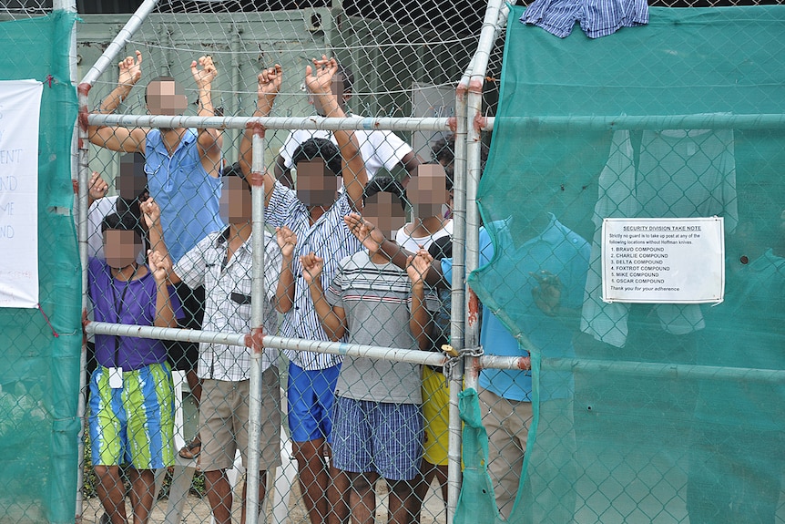 Asylum seekers stare at media from behind a fence