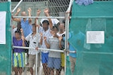 Asylum seekers stare from behind fence