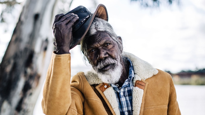 Actor David Gulpilil, an older Yolngu man in shearling coat taking off his akubra, in the documentary My Name is Gulpilil