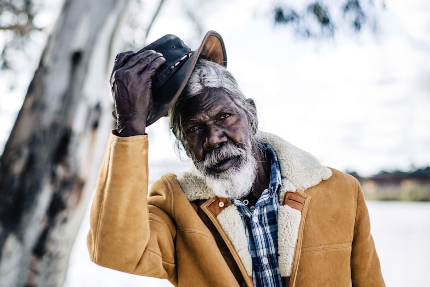 Actor David Gulpilil, an older Yolngu man in shearling coat taking off his akubra, in the documentary My Name is Gulpilil