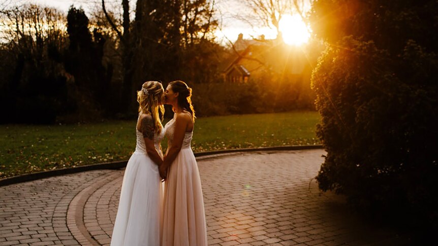 Two women in wedding dresses kissing