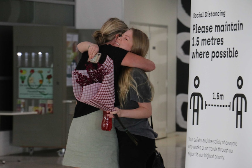 Two women hug at Perth Airport in front of a social distancing reminder sign