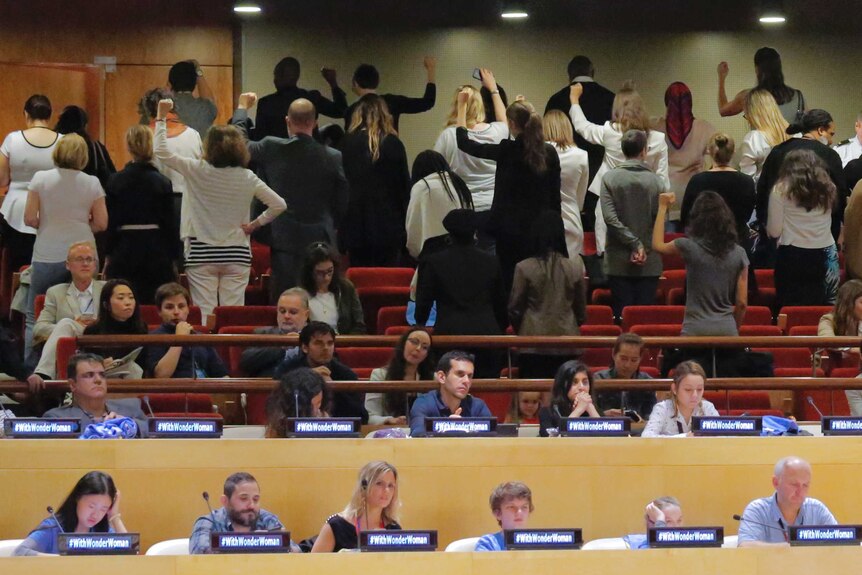 UN staff silently turn their back to the stage, some with their fists in the air.