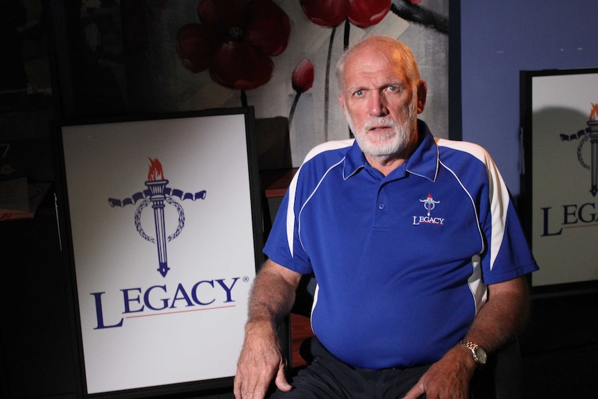 Man sits in dim lighting with Legacy sign on his left-hand side .