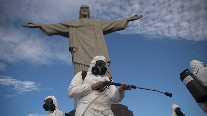 Soldiers in hazmat suits disinfect the Christ the Redeemer statue using hoses attached to backpacks.