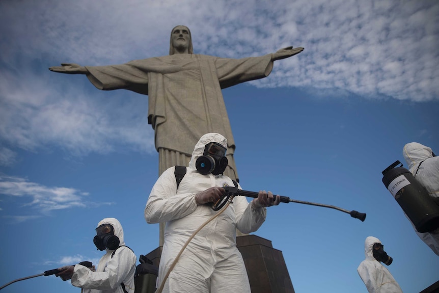 Soldiers in hazmat suits disinfect the Christ the Redeemer statue using hoses attached to backpacks.