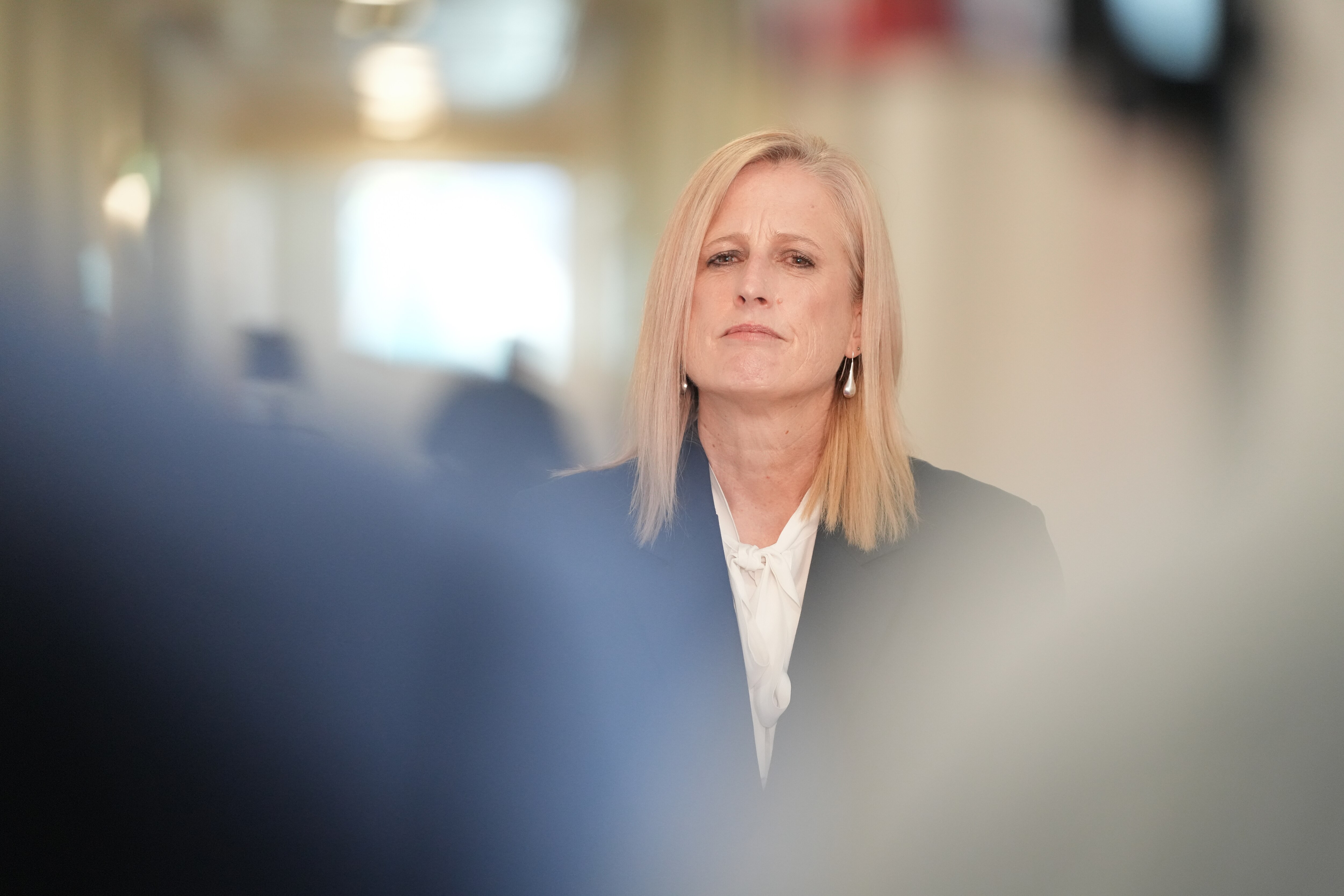 Uma mulher com cabelos loiros na altura do queixo tem uma expressão séria.