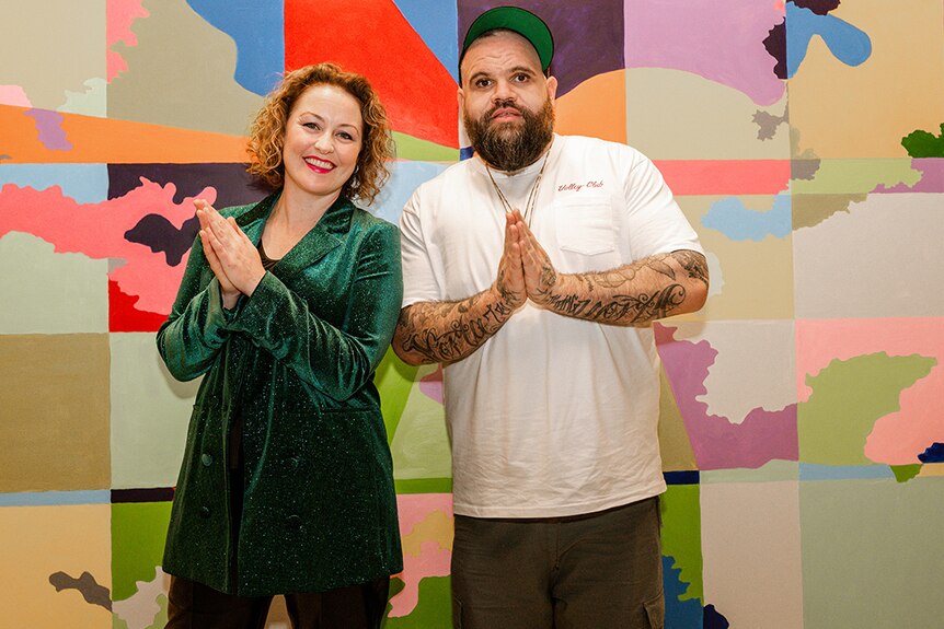 Briggs and Zan Rowe stand with the hands clasped in front of a colourful wall at the Shepparton Art Museum