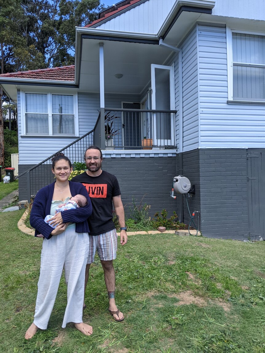 a couple with a baby in front of a house
