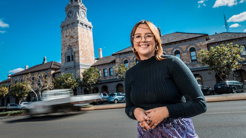 Teri Campbell, standing in front of the Kalgoorlie courthouse and town clock, on a bright sunny day.