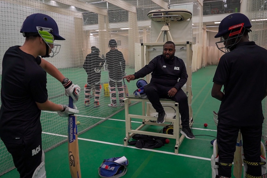 Chevy Green talks to two young boys in cricket batting equipment.