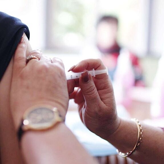 close up of ladies hands administering a flu vaccination into persons arm with rolled up sleeve