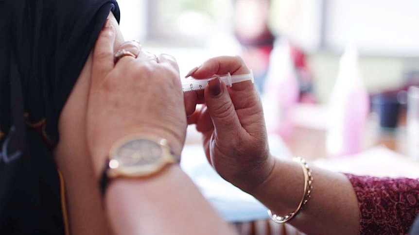 close up of ladies hands administering a flu vaccination into persons arm with rolled up sleeve