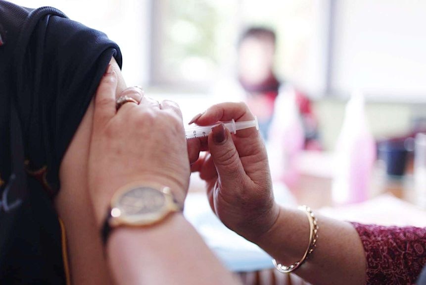 A woman administers a flu shot in someone's arm.