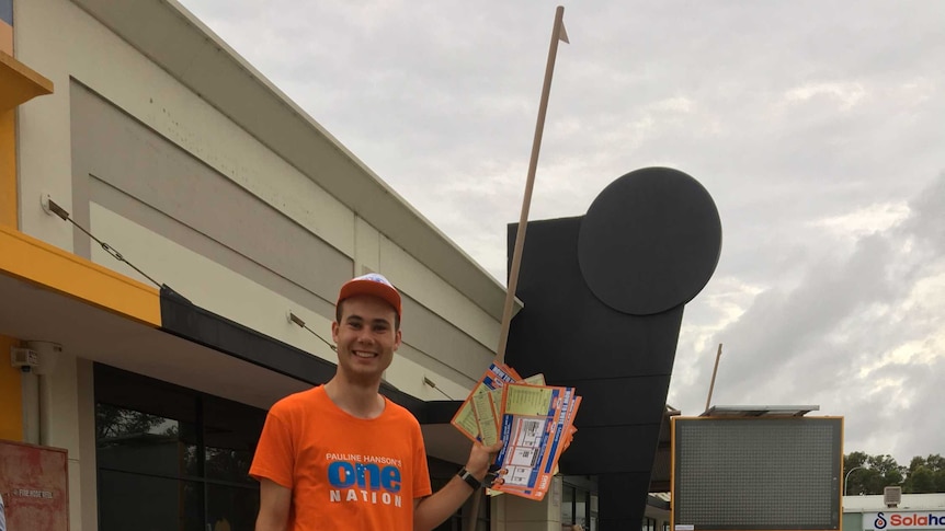 Tyler Walsh, a  young man is standing next to a placard that has a photo of Pauline Hanson and himself on it. He is campaigning.
