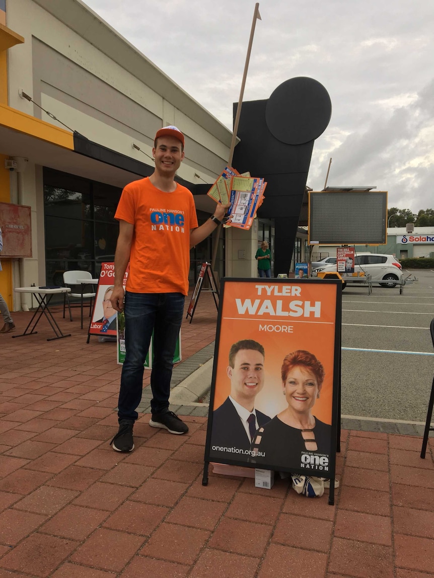 Tyler Walsh, a  young man is standing next to a placard that has a photo of Pauline Hanson and himself on it. He is campaigning.