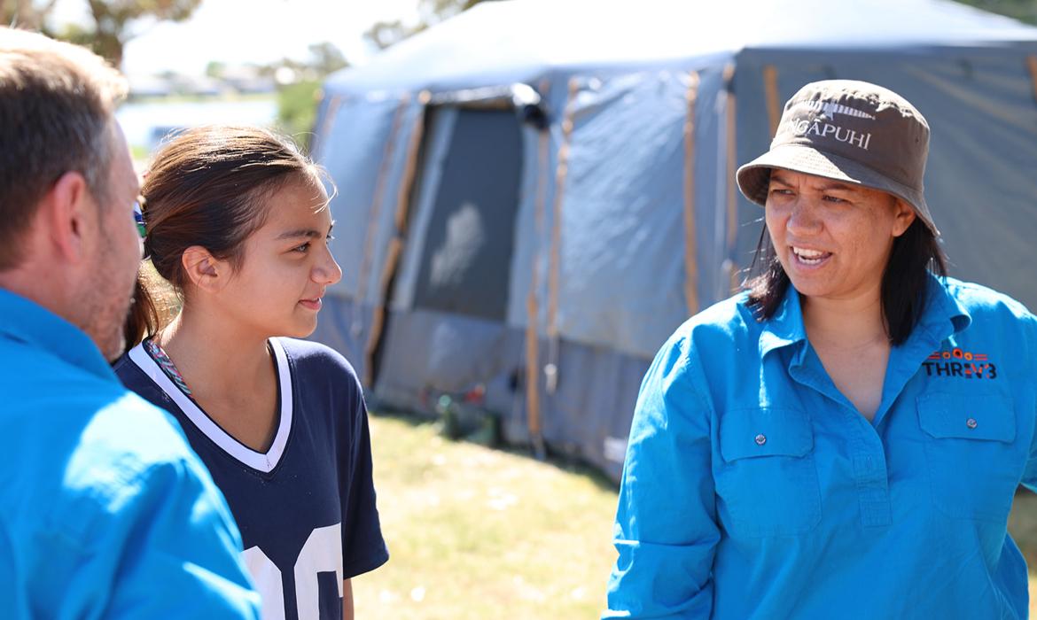 A woman speaks to a girl while standing outside a tent.