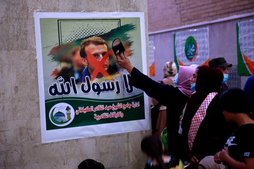 A woman hits a poster with a defaced picture of French President Emmanuel Macron with a shoe.