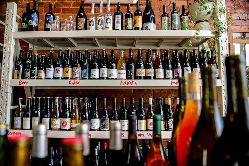 Wine store with shelf of brightly coloured natural wine in front of exposed brick wall