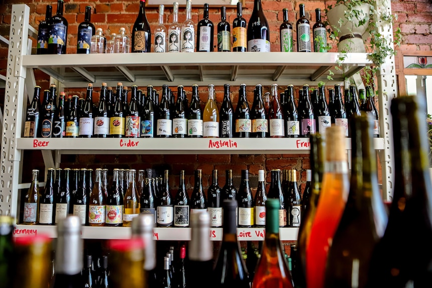 Wine store with shelf of brightly coloured natural wine in front of exposed brick wall