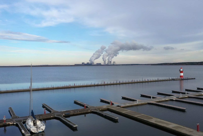 A lake with boats in the foreground and a smokestack in the background.