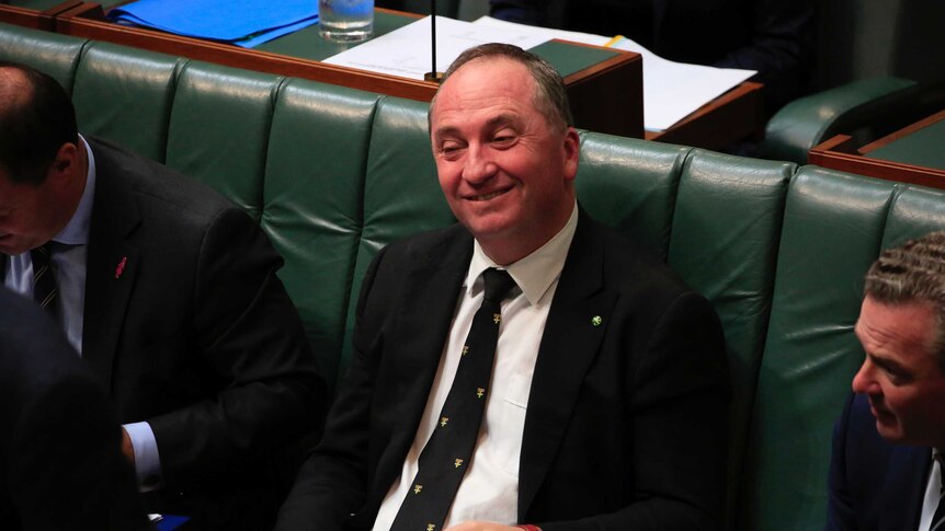 Barnaby Joyce smiles and listens during question time while holding papers in his lap.