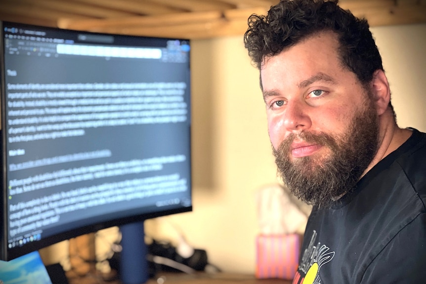 Disabled university student Adam Whitehead sitting in front of a large computer screen