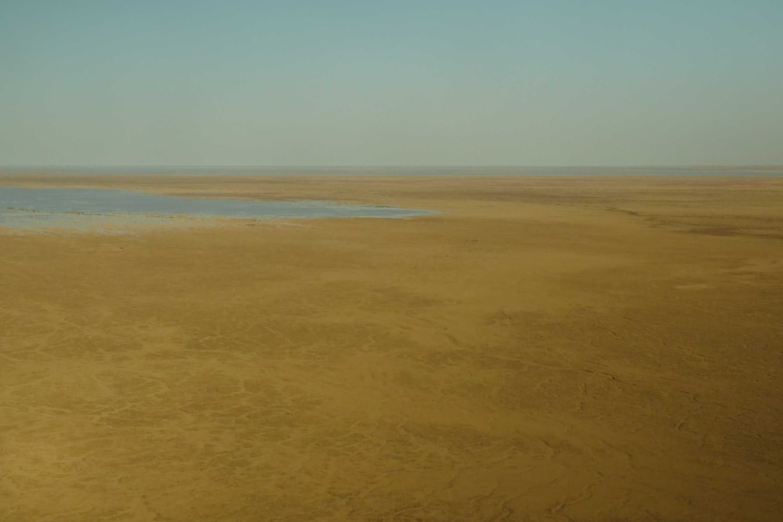 An expanse of flat, bare ground with a body of water moving in from the left.