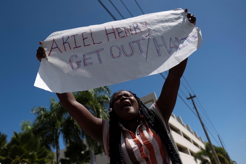 A female protestor holds up a sign saying "Ariel Henry get out"