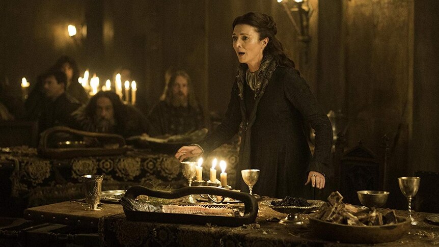 A woman stands up from a table in panic in a scene from a fantasy tv show