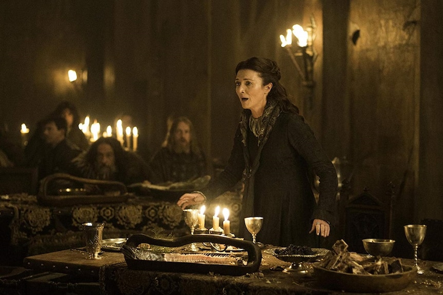 A woman stands up from a table in panic in a scene from a fantasy tv show