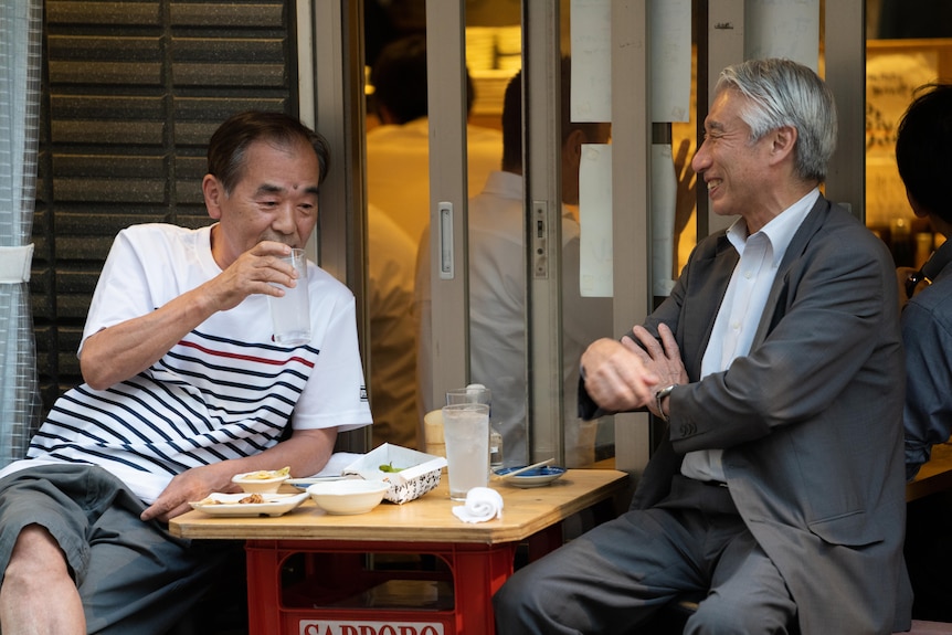 Two older Japanese men enjoying a drink at an outdoor table in Tokyo 