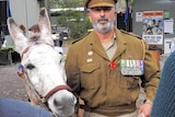 A man in an Australian military uniform stands with a donkey