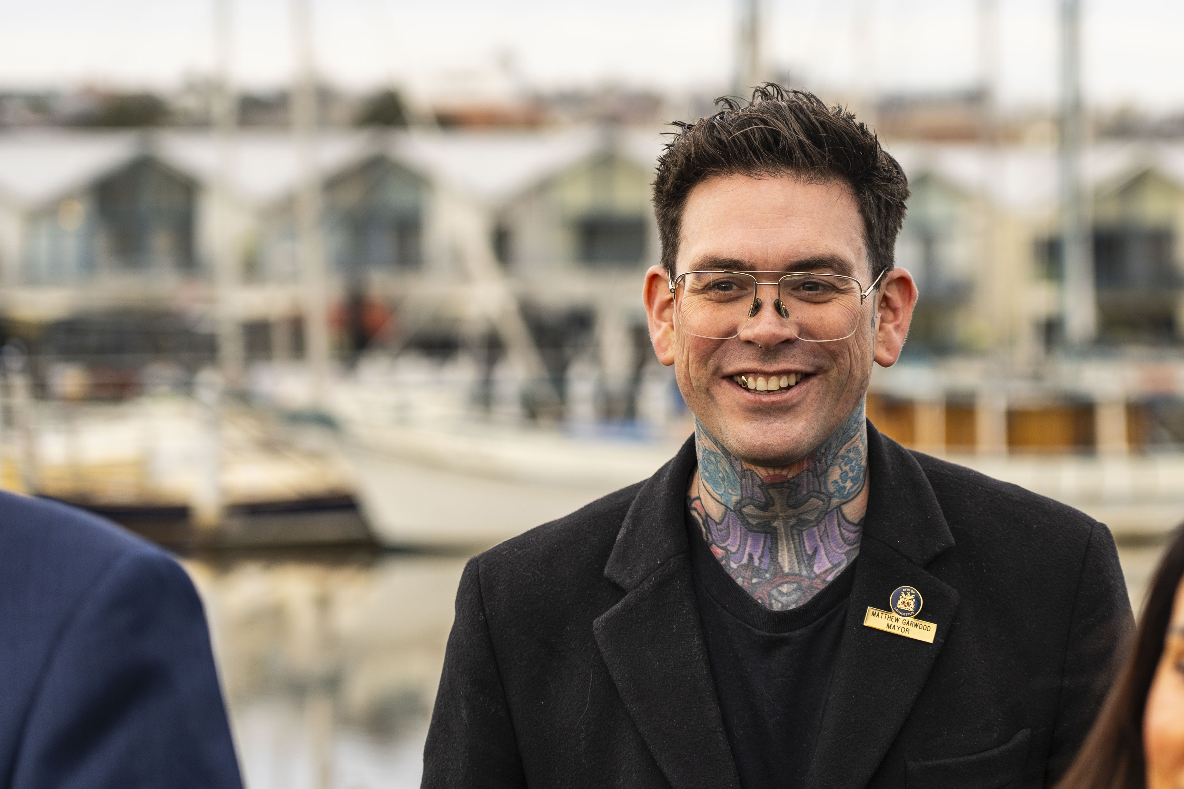 a man wears black and and glasses and has tattoos up his neck