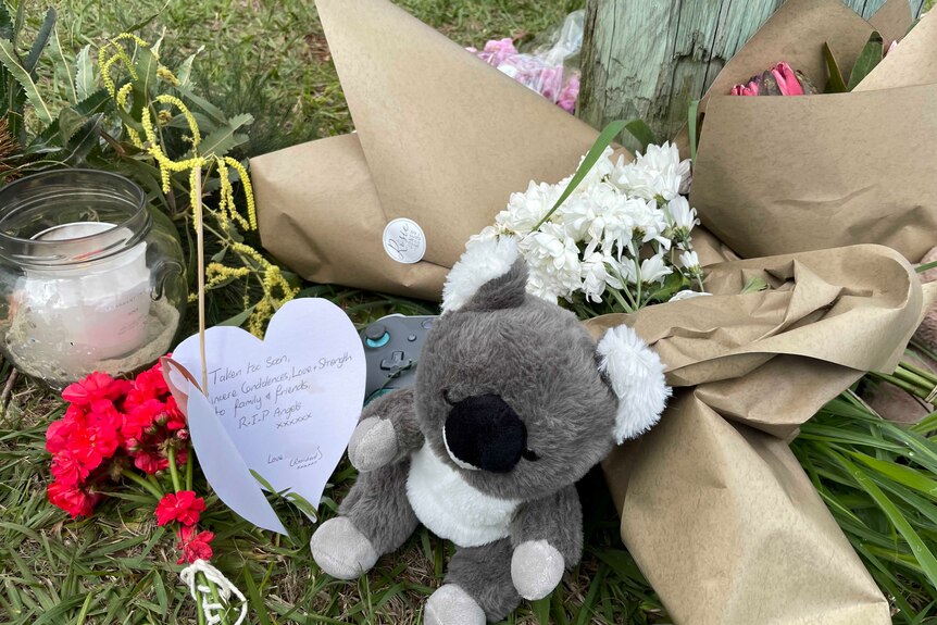 Memorial of flowers and game controller handset and plush koala toy near Russell Island house fire scene