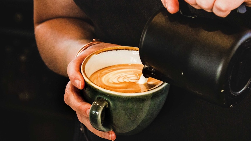 A woman pours milk into a mug of coffee.