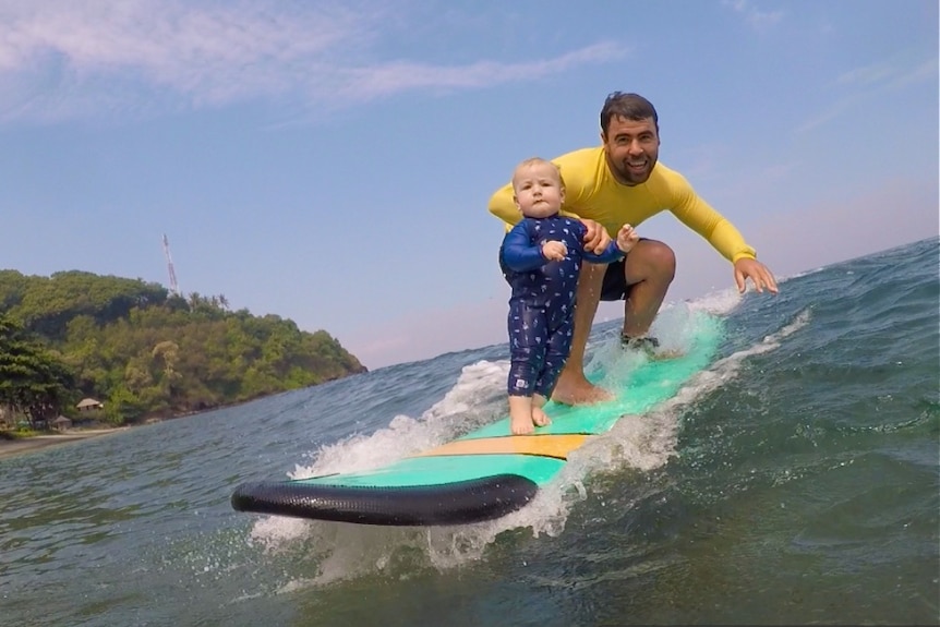 A toddler with a man on a surfboard.