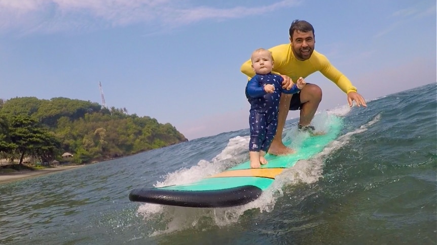 A toddler with a man on a surfboard.