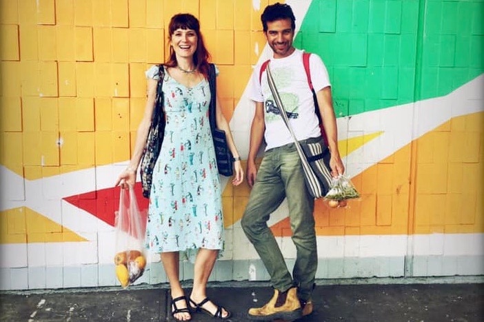 A woman and a man stand smiling in front of a multicoloured wall.
